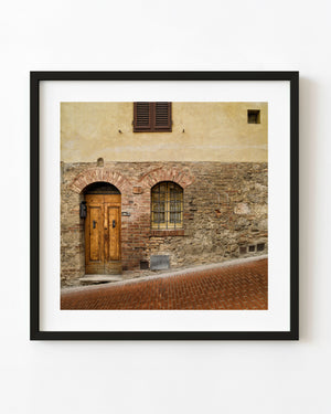 Arched wooden doorway and barred window in a weathered Tuscan stone wall.