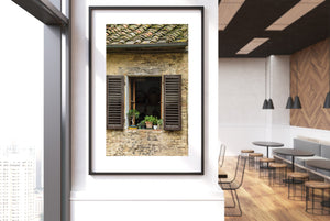 Green plants brighten a stone facade with brown louvred shutters in Tuscany.