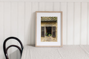 Vertical Tuscan architectural photograph of plants, shutters and textured stone.