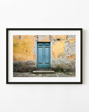 Weathered blue double door surrounded by peeling ochre plaster in Tuscany.