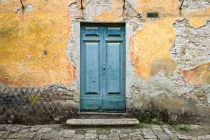 Blue wooden doorway contrasts with golden plaster and exposed stone on a Tuscan facade.