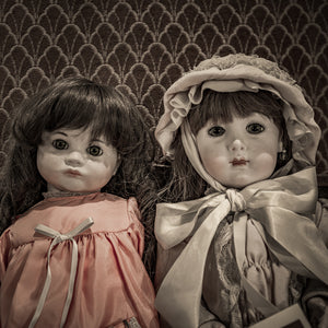 Porcelain dolls with glassy eyes, lace details and ribbon bows in a muted still life.