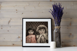 An antique doll in a bonnet sits beside a smaller long-haired porcelain doll.