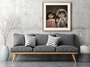 Two vintage dolls with ribboned clothing and dark hair against textured upholstery.