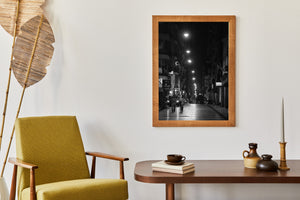 Dark storefronts frame pedestrians and pools of light on a nighttime street.