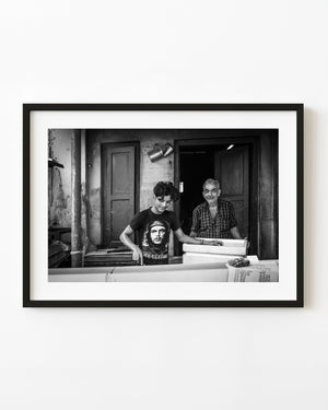 Two men at work behind a counter in Kochi India, photographed in black and white.