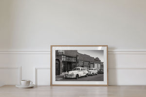 Black and white photograph of vintage American cars on quiet small town street