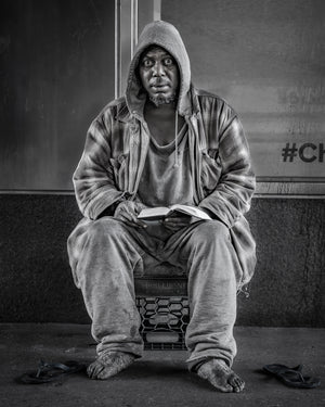 Monochrome portrait of barefoot man sitting on sidewalk reading
