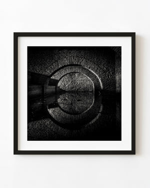 Brick arches reflected in still water inside a Uruguay reservoir in black and white