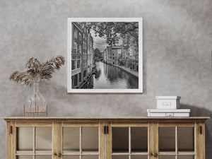 Monochrome canal scene with tall windows, waterside paths and leafy branches