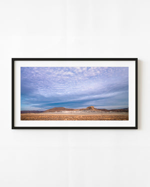 Vast cloud-filled sky above layered desert mesas and dry grassland