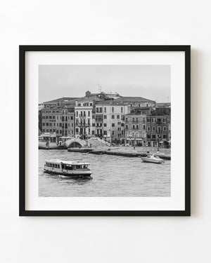 Venice canal boat passing historic waterfront buildings in black and white