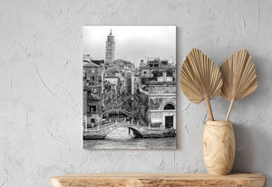 A tall campanile rises beyond Venice rooftops and winding canal crossings