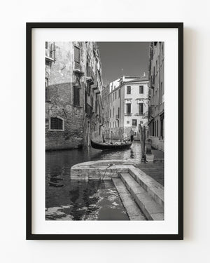 Gondola carrying passengers through a narrow Venice canal in black and white