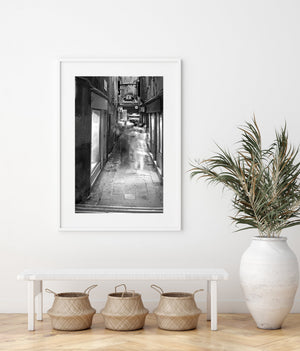 Black and white view down a busy Venetian laneway with moving figures