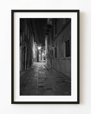 Empty Venice laneway lit by starburst streetlights at night in black and white