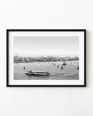 Venice waterbus crossing open water beside channel markers in black and white