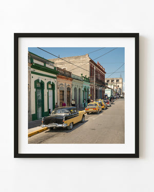 Classic cars and yellow taxis beside colorful Cuban main-street buildings