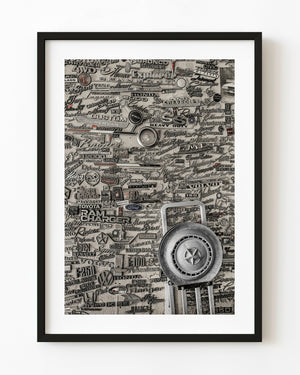 Vintage automotive emblems cover a wall behind a large hubcap in toned monochrome