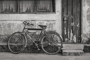 An old bicycle rests below a barred window beside a peeling wooden doorway