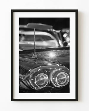 Chrome antenna above paired vintage car tail lights in black and white