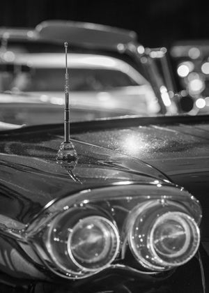 A slender car antenna stands sharply against soft reflections and blurred chrome
