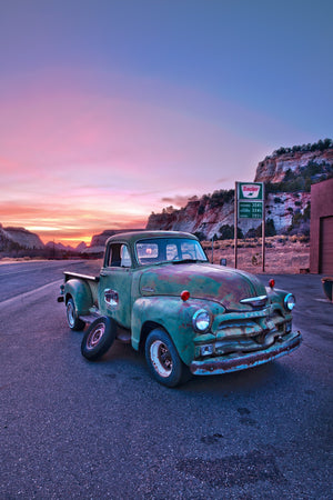 Vintage Chevrolet truck parked near red cliffs and a Sinclair sign at sunset