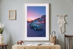 A vintage pickup and spare tire beside a quiet Southwestern road at dusk