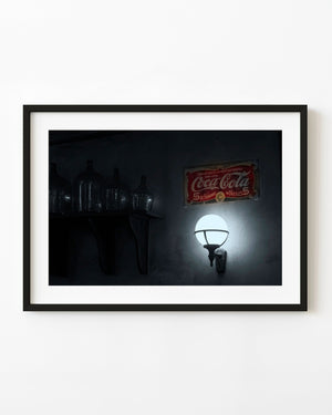 Vintage red Coca-Cola sign above a glowing globe lamp and dark glass bottles