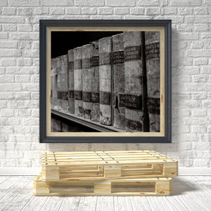 Framed black and white photo of stacked books on a brick wall with a wooden pallet at the bottom.