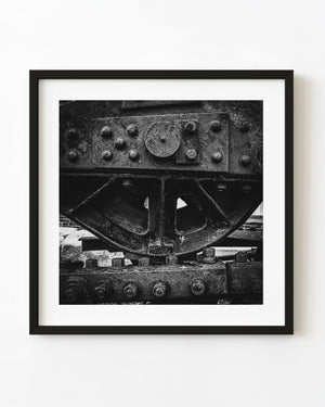 Dark industrial machinery with a large wheel and heavy bolts in monochrome.
