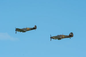 Camouflaged RAF aircraft pair in flight beneath open blue sky.