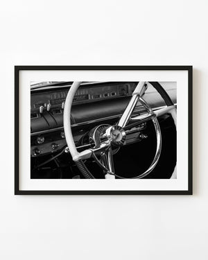 Vintage car steering wheel and dashboard in black and white.