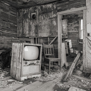 Black and white farmhouse interior with an old television and fallen plaster.