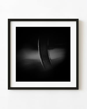 Wagon wheel rim emerging from deep shadow in black and white.