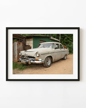 Weathered cream classic car parked beside a green building in Cuba
