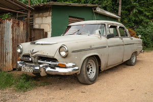 Cream vintage car with chrome bumpers on a Cuban dirt lane