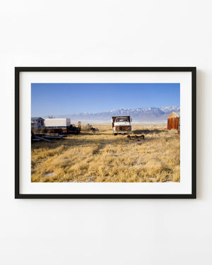 Weathered farm truck and equipment beneath snow-covered mountains