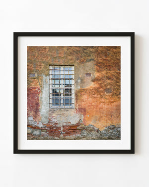 Barred window on a weathered ochre Italian wall