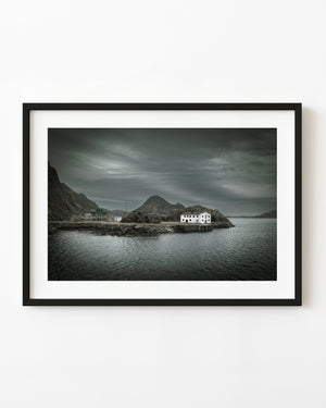Weathered white waterfront building beneath dark clouds in Lofoten
