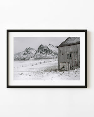 Weathered Norwegian barn beside snow-covered Lofoten mountains