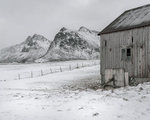 Antiguo granero de madera y paisaje montañoso nevado en Flakstad, Noruega