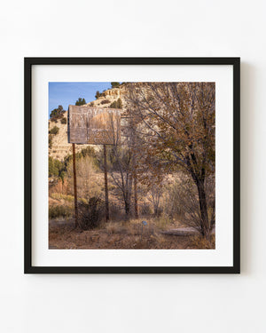 Weathered RV Tours sign among trees beneath pale Utah cliffs