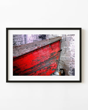 Weathered red rowboat hull leaning against a pale brick wall