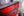 Peeling red paint on a wooden rowboat beside textured brickwork