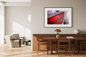 Close-up of an old red rowboat hull against a weathered masonry wall