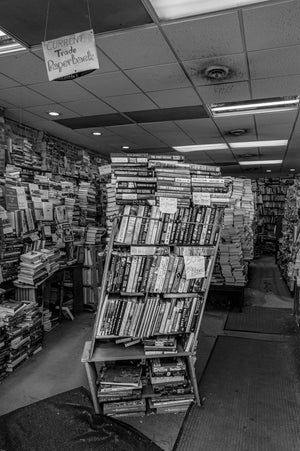 Stacks of books in a bookstore with a sign on the ceiling.