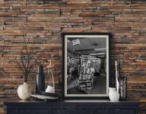 Framed black and white photo of a bookshelf against a wooden wall with decorative items.