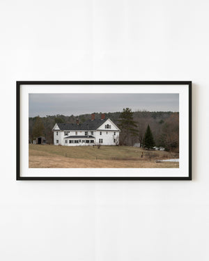 White Maine house in an early spring landscape beneath a grey sky