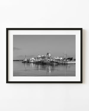 Tugboats moored beside waterfront buildings with reflections in black and white